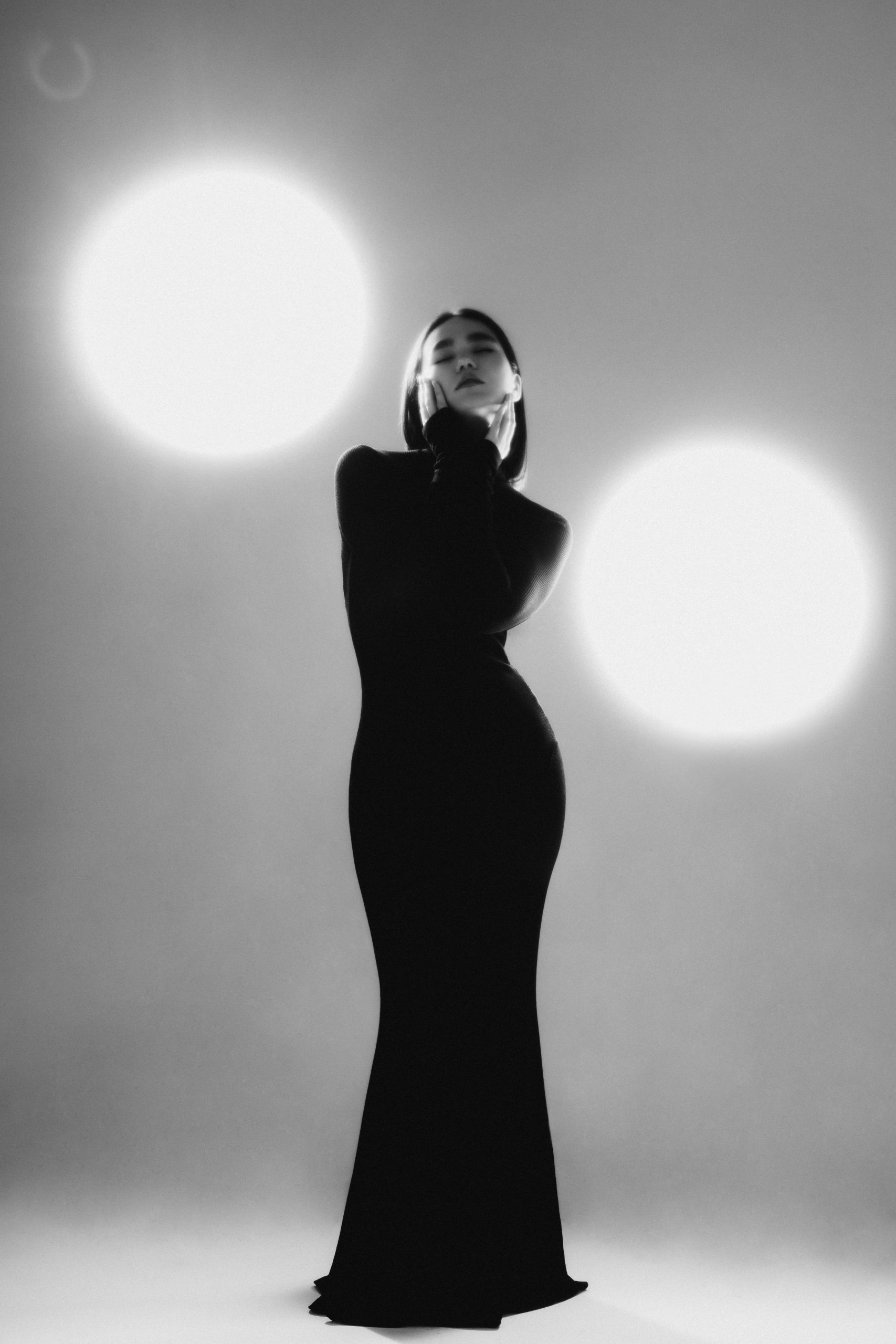 Fashion portrait of a woman in a long black dress, studio lighting, elegant pose.