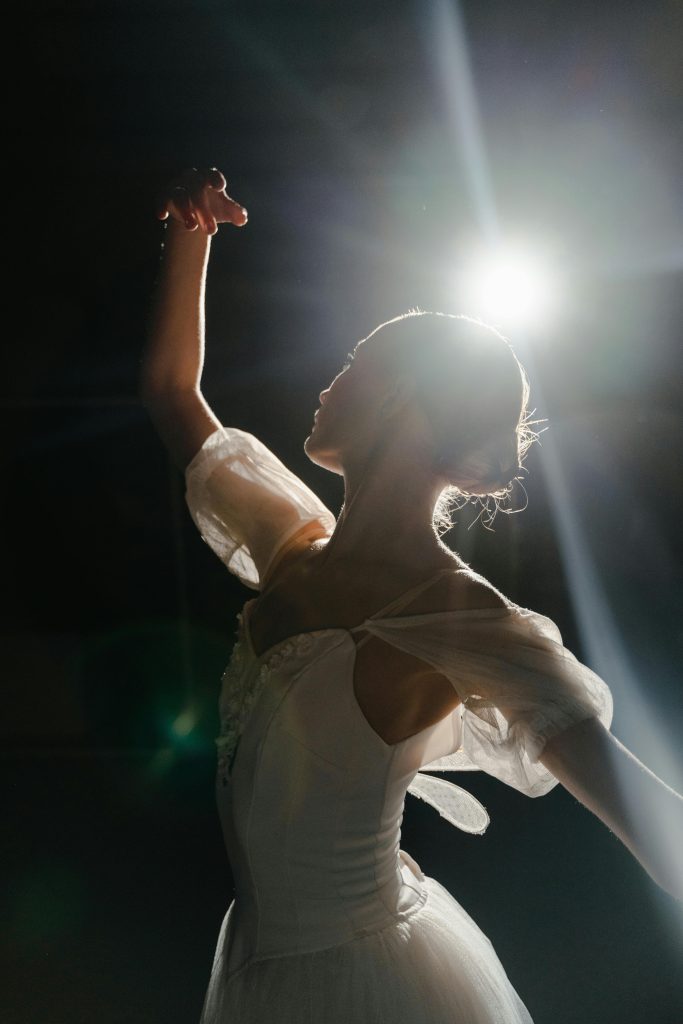 Silhouette of a ballet dancer in a white costume gracefully posing under spotlight.